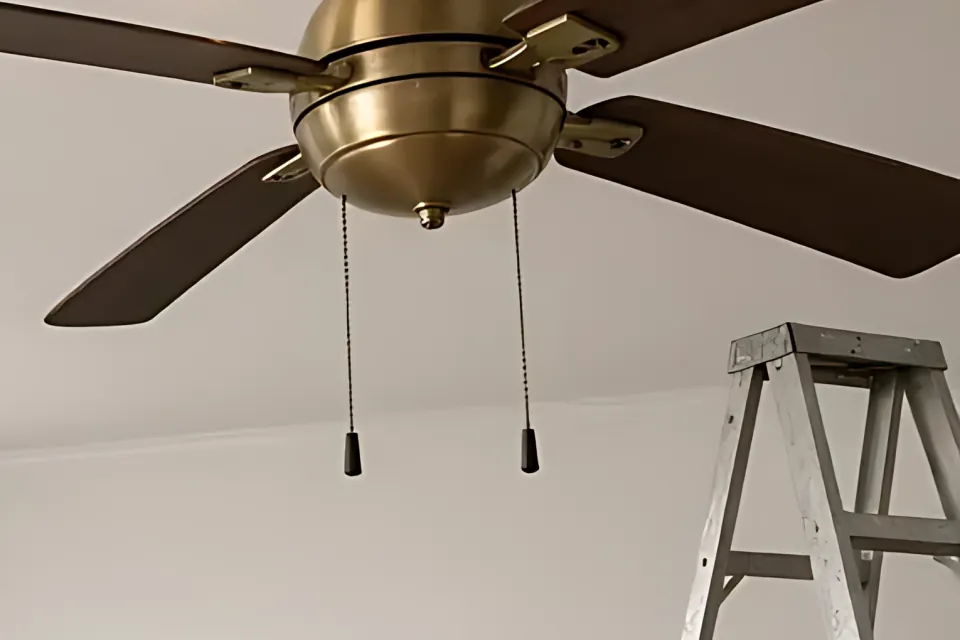 Close-up of a ceiling fan with pull chains and a step ladder below.