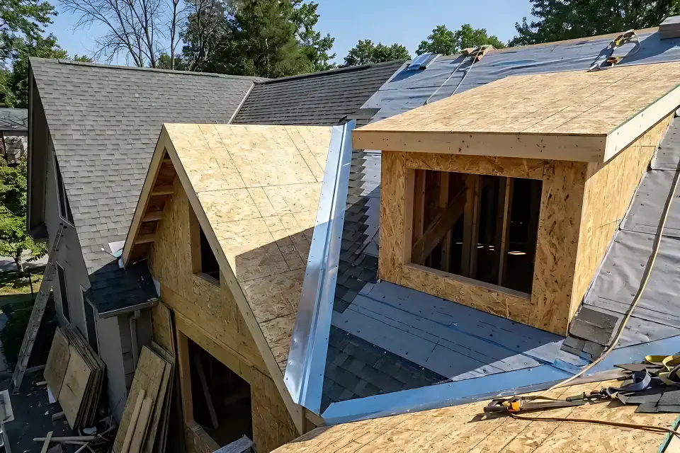 Residential roof renovation showing a newly framed shed dormer and gable roof extension tied into an existing asphalt-shingle roof with metal valley flashing and OSB sheathing.