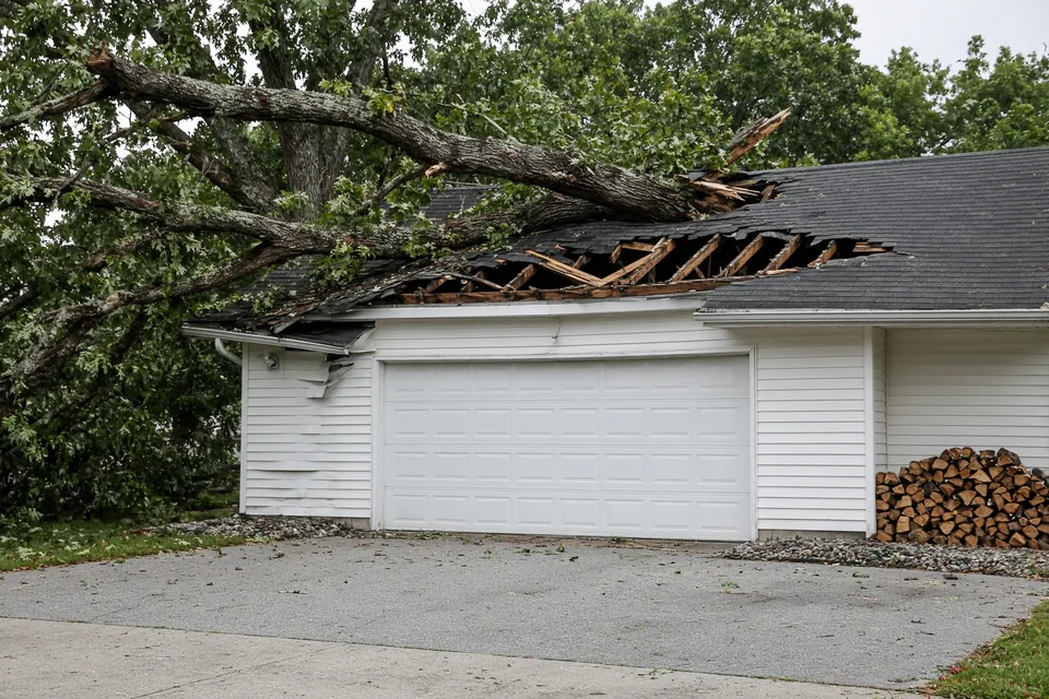Detached residential garage with a fallen oak limb crushing the shingle roof ridge.
