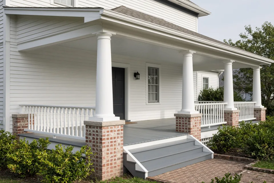Covered American front porch with four white structural columns, tongue-and-groove floor, and wood railings.