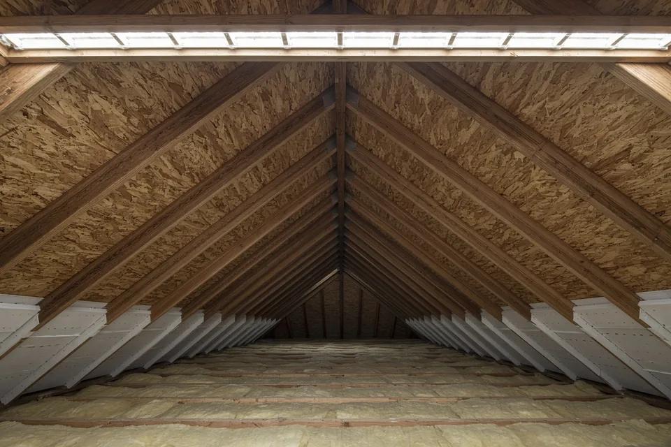 Attic view showing daylight along the continuous open ridge vent slot at the peak and rafter baffles at the eave.