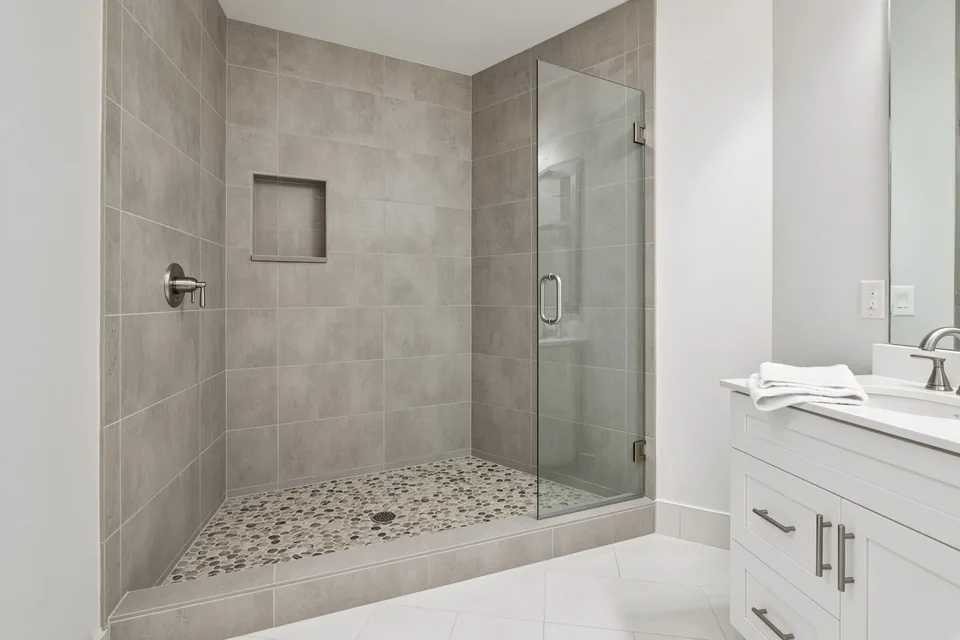 Completed 60-inch alcove walk-in shower with porcelain tile walls, mosaic floor, and frameless glass door.